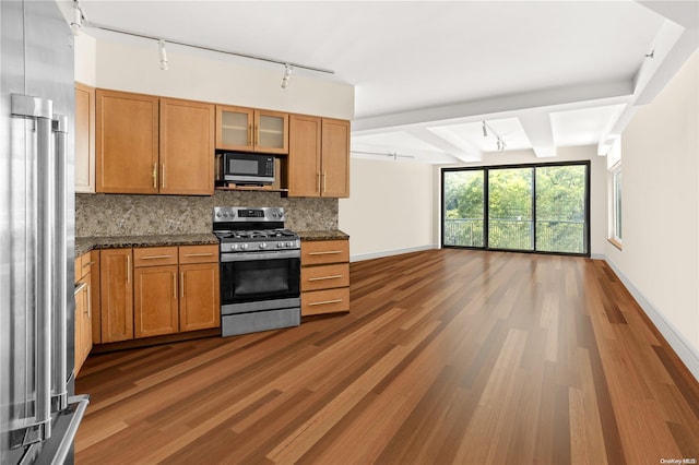 kitchen with rail lighting, dark stone countertops, beam ceiling, dark hardwood / wood-style flooring, and stainless steel appliances