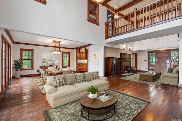 living room with a high ceiling, dark hardwood / wood-style floors, ornamental molding, and beam ceiling