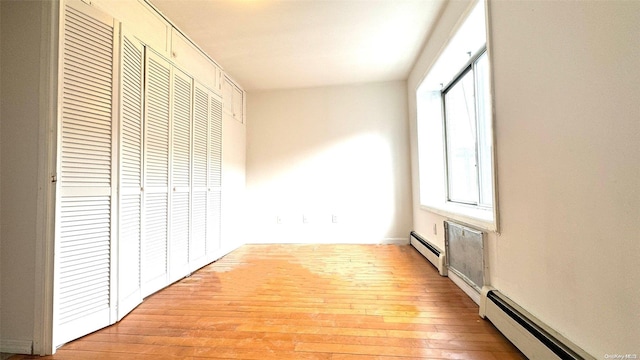 unfurnished bedroom featuring light wood-type flooring, a closet, and a baseboard heating unit