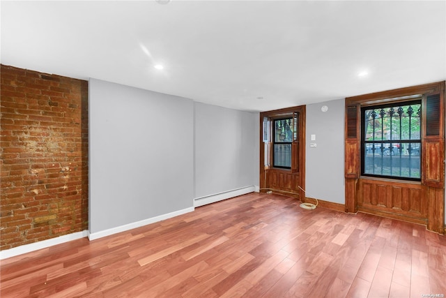 empty room with light hardwood / wood-style floors, brick wall, and a baseboard heating unit