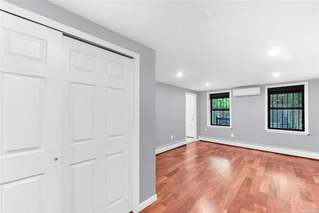 empty room with wood-type flooring, a wall unit AC, and a baseboard heating unit