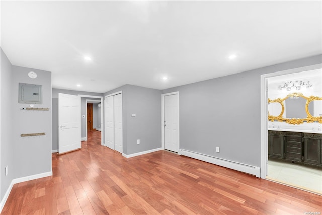 unfurnished living room featuring light hardwood / wood-style floors, baseboard heating, and electric panel