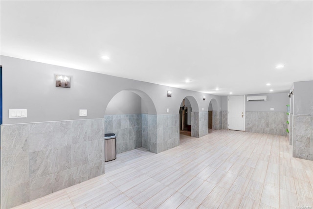 unfurnished living room with an AC wall unit and tile walls