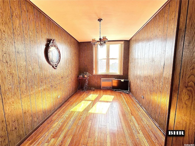 empty room with radiator, wooden walls, light hardwood / wood-style flooring, and an inviting chandelier