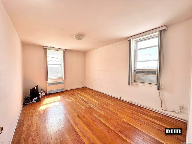 empty room featuring cooling unit, radiator, and light hardwood / wood-style flooring