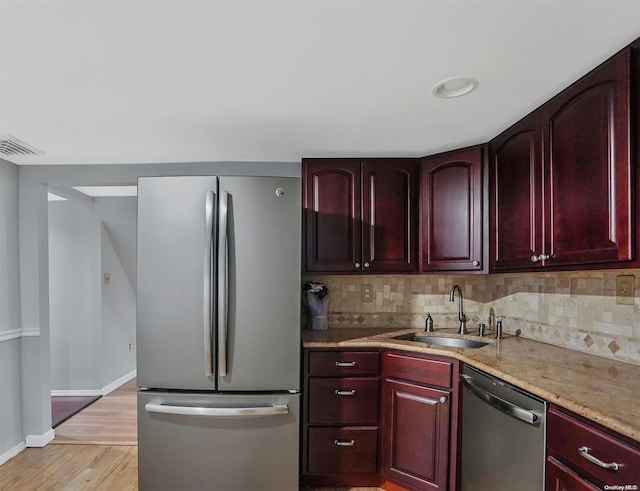 kitchen with appliances with stainless steel finishes, light wood-type flooring, tasteful backsplash, light stone counters, and sink