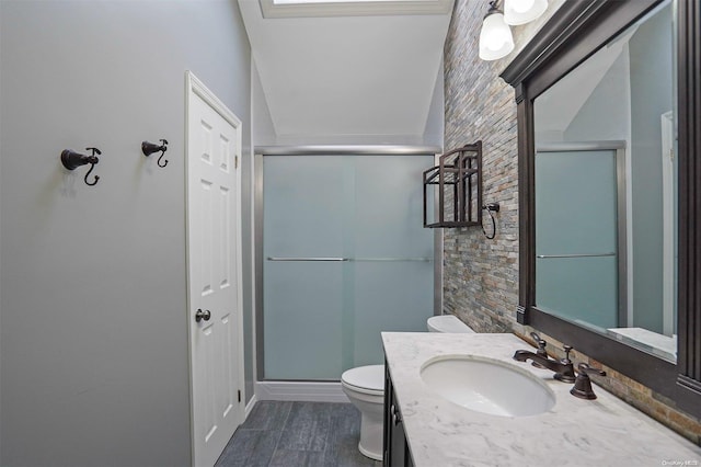 bathroom featuring lofted ceiling, toilet, a shower with shower door, and vanity