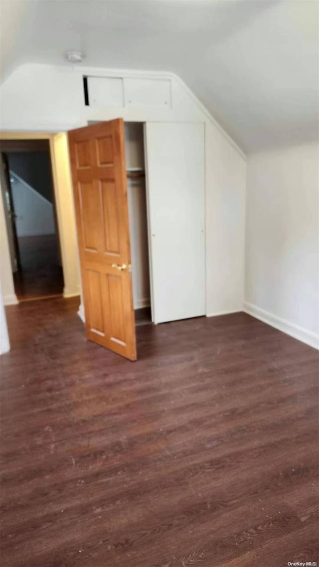 unfurnished bedroom with dark hardwood / wood-style flooring, lofted ceiling, and a closet