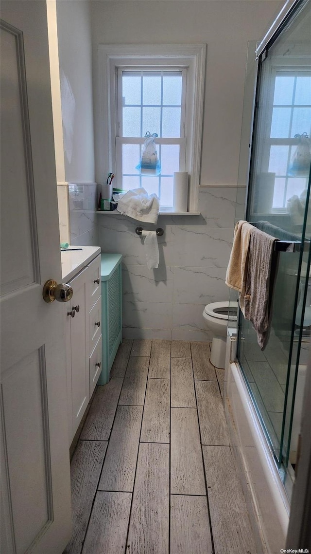 full bathroom featuring vanity, toilet, bath / shower combo with glass door, and tile walls