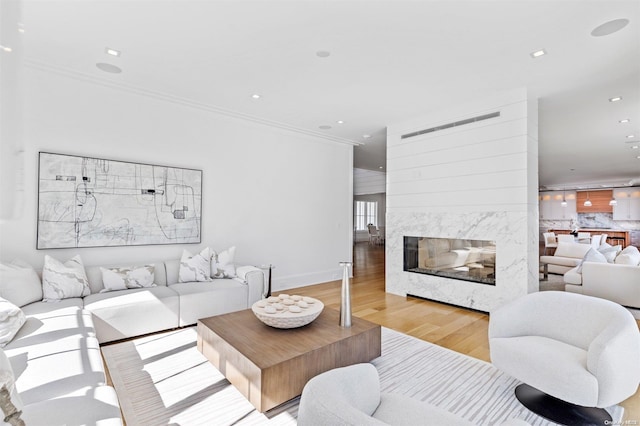 living room featuring light wood-type flooring, ornamental molding, and a high end fireplace