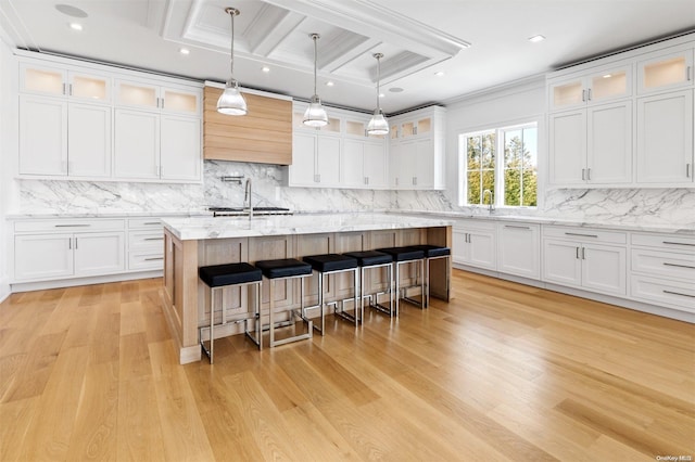 kitchen with white cabinets, beam ceiling, light hardwood / wood-style floors, and an island with sink