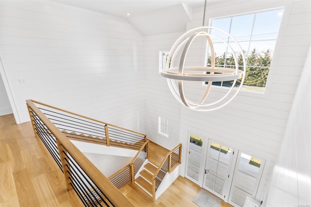 stairs with wood walls, wood-type flooring, vaulted ceiling, and a notable chandelier