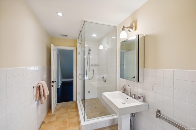 bathroom featuring tile patterned flooring, sink, a shower with shower door, and tile walls