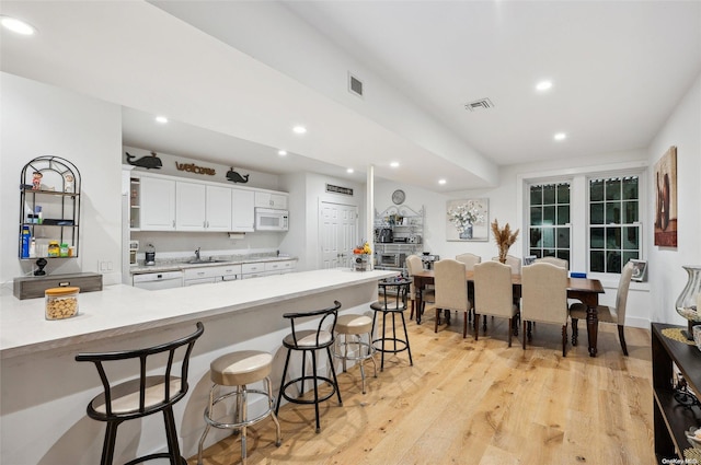 kitchen with light hardwood / wood-style flooring, kitchen peninsula, white appliances, a breakfast bar area, and white cabinets