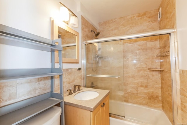 full bathroom featuring shower / bath combination with glass door, tile walls, backsplash, vanity, and toilet