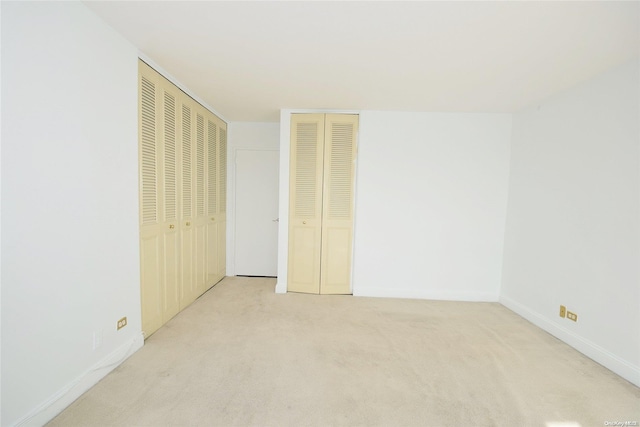 unfurnished bedroom featuring light carpet and two closets