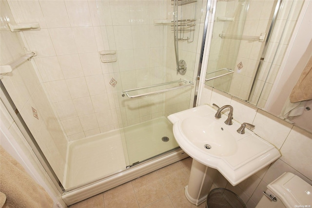 bathroom featuring tile patterned floors, toilet, a shower with door, and tile walls