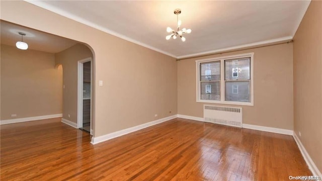 spare room featuring hardwood / wood-style flooring, an inviting chandelier, radiator, and crown molding