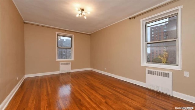 spare room with radiator heating unit, hardwood / wood-style flooring, and a healthy amount of sunlight