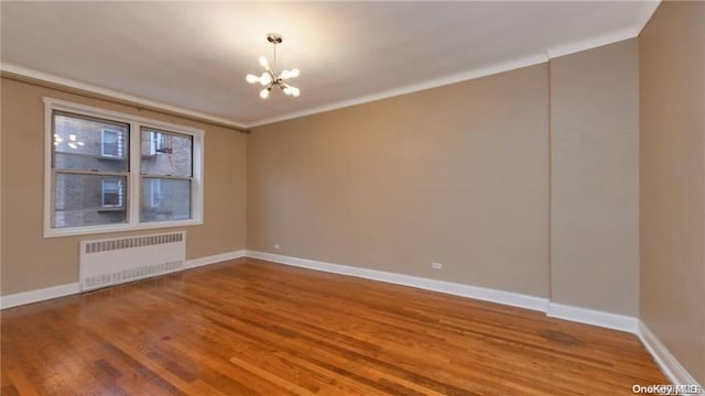 spare room featuring hardwood / wood-style floors, crown molding, radiator, and a notable chandelier