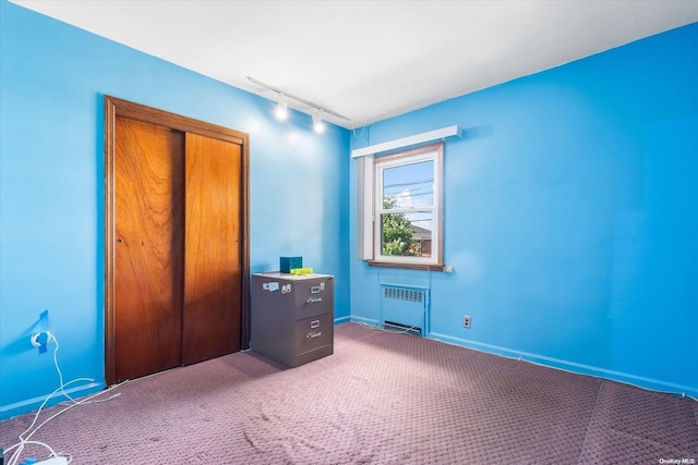 unfurnished bedroom featuring carpet floors, radiator, a closet, and rail lighting