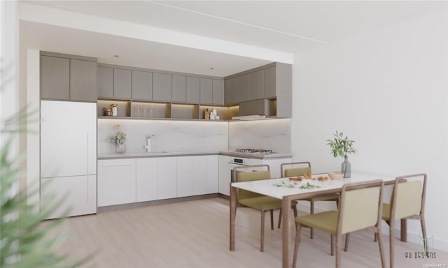 kitchen with gray cabinetry, sink, wall chimney range hood, light hardwood / wood-style floors, and stainless steel gas stovetop