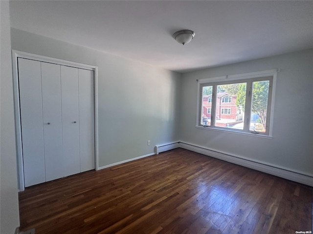 unfurnished bedroom with a closet, dark wood-type flooring, and a baseboard heating unit