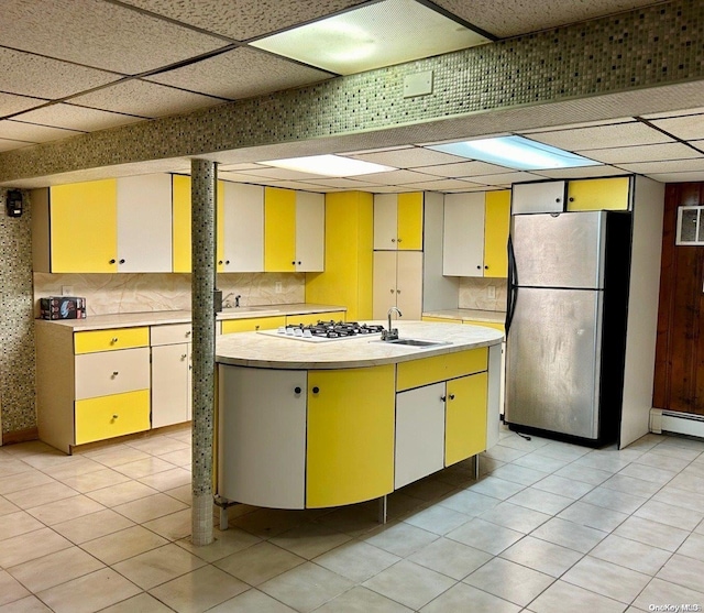 kitchen featuring stainless steel fridge, a drop ceiling, light tile patterned floors, and a center island with sink