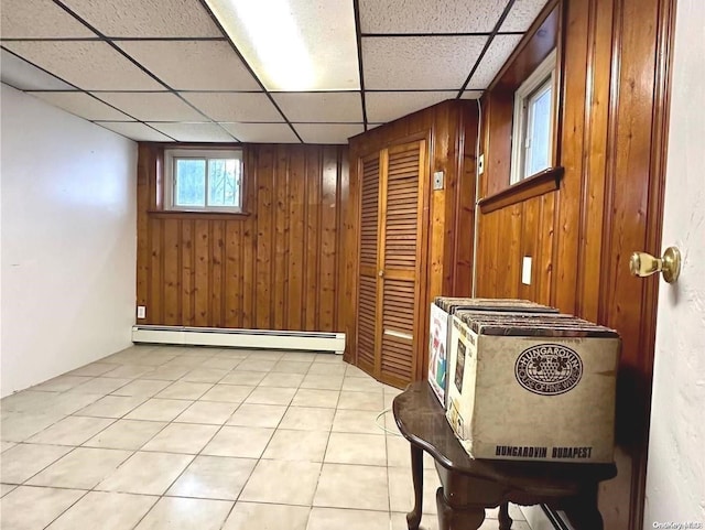 interior space featuring a drop ceiling, wood walls, and baseboard heating