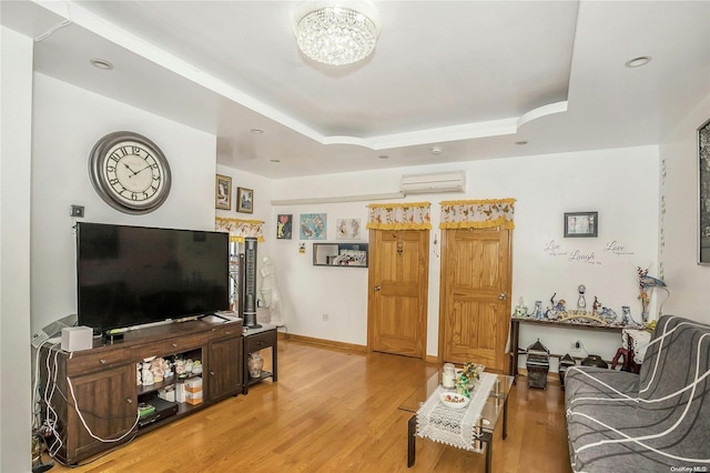 living room with an inviting chandelier, hardwood / wood-style flooring, a raised ceiling, and a wall unit AC