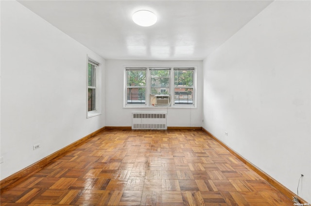 empty room featuring radiator heating unit, light parquet floors, and cooling unit