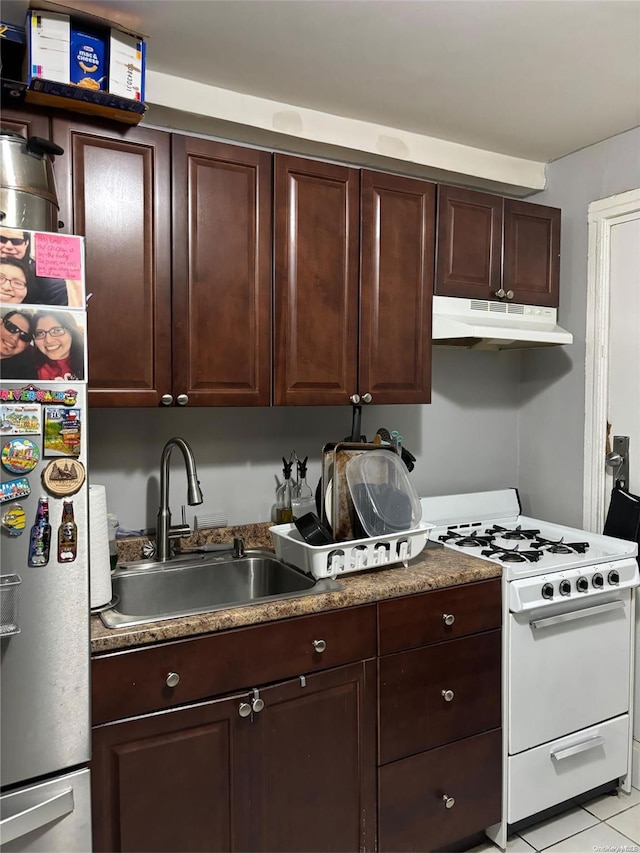 kitchen with dark brown cabinetry, sink, white range oven, stainless steel fridge, and light tile patterned floors