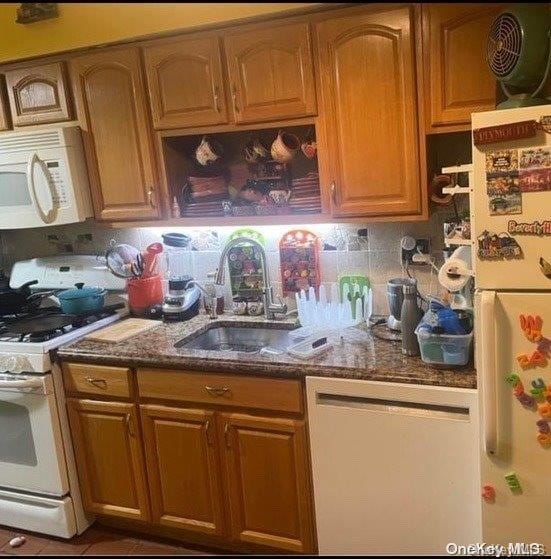 kitchen featuring white appliances, tasteful backsplash, dark stone counters, and sink