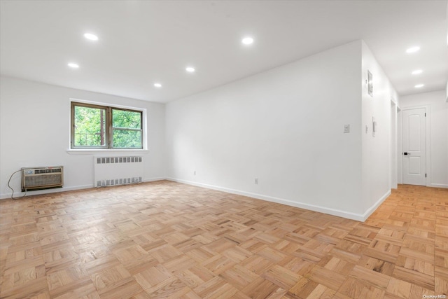 spare room with radiator heating unit, light parquet flooring, and a wall unit AC