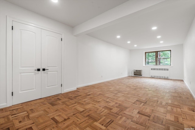 unfurnished living room featuring beamed ceiling, radiator heating unit, light parquet floors, and an AC wall unit