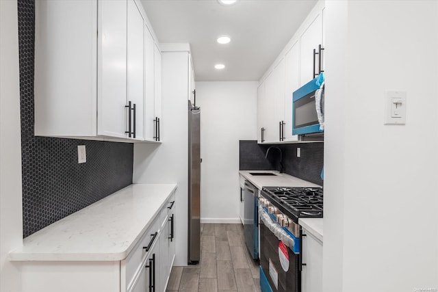 kitchen with backsplash, sink, light wood-type flooring, white cabinetry, and stainless steel appliances