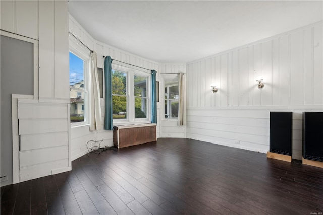 unfurnished living room with wooden walls, radiator, and dark wood-type flooring