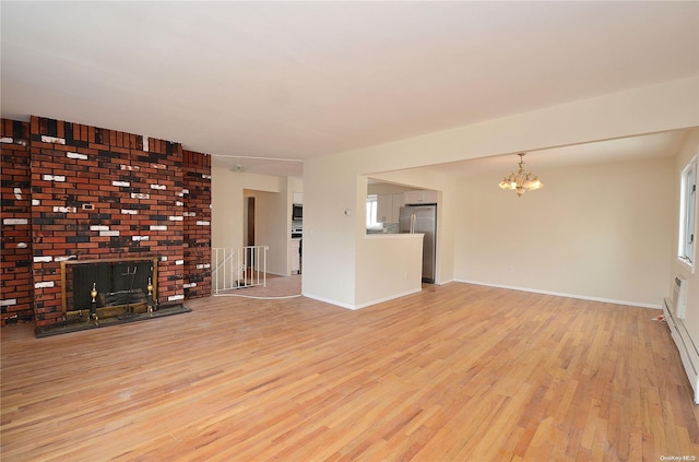 unfurnished living room with a notable chandelier, light hardwood / wood-style floors, and a brick fireplace