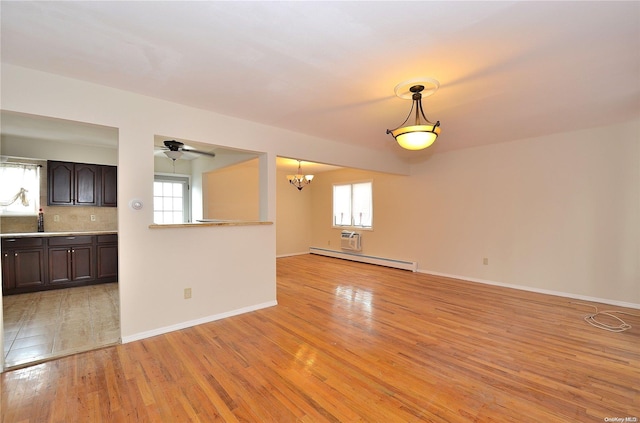 unfurnished living room with ceiling fan with notable chandelier, a baseboard radiator, and light hardwood / wood-style floors