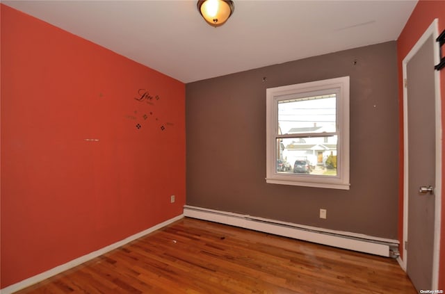 unfurnished room with wood-type flooring and a baseboard heating unit