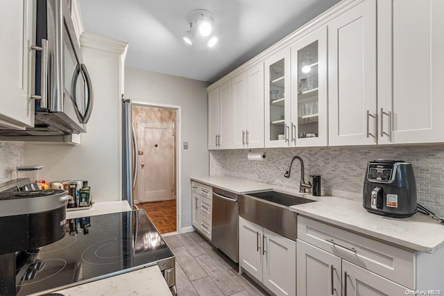 kitchen featuring white cabinets, sink, light stone countertops, light wood-type flooring, and appliances with stainless steel finishes