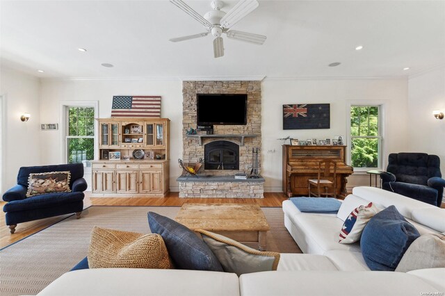 living room featuring a fireplace, light wood-type flooring, ceiling fan, and crown molding