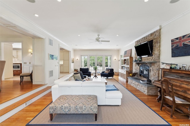 living room featuring ceiling fan, a stone fireplace, light wood-type flooring, and ornamental molding