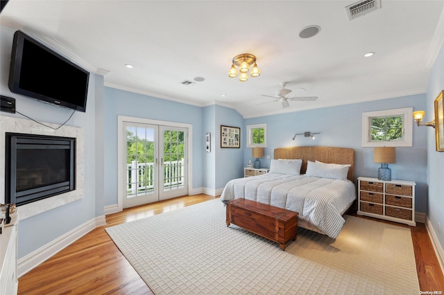 bedroom with access to exterior, ceiling fan, a premium fireplace, light wood-type flooring, and ornamental molding