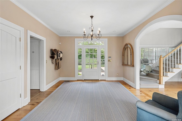 foyer entrance with crown molding, a notable chandelier, and light wood-type flooring