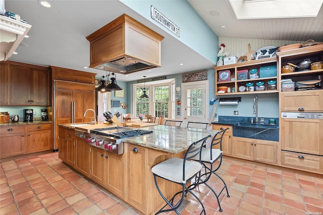 kitchen with custom exhaust hood, a kitchen island with sink, light stone countertops, a kitchen bar, and stainless steel gas cooktop