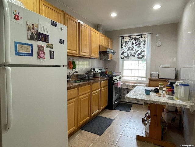 kitchen featuring stainless steel gas range oven, backsplash, white refrigerator, sink, and light tile patterned floors