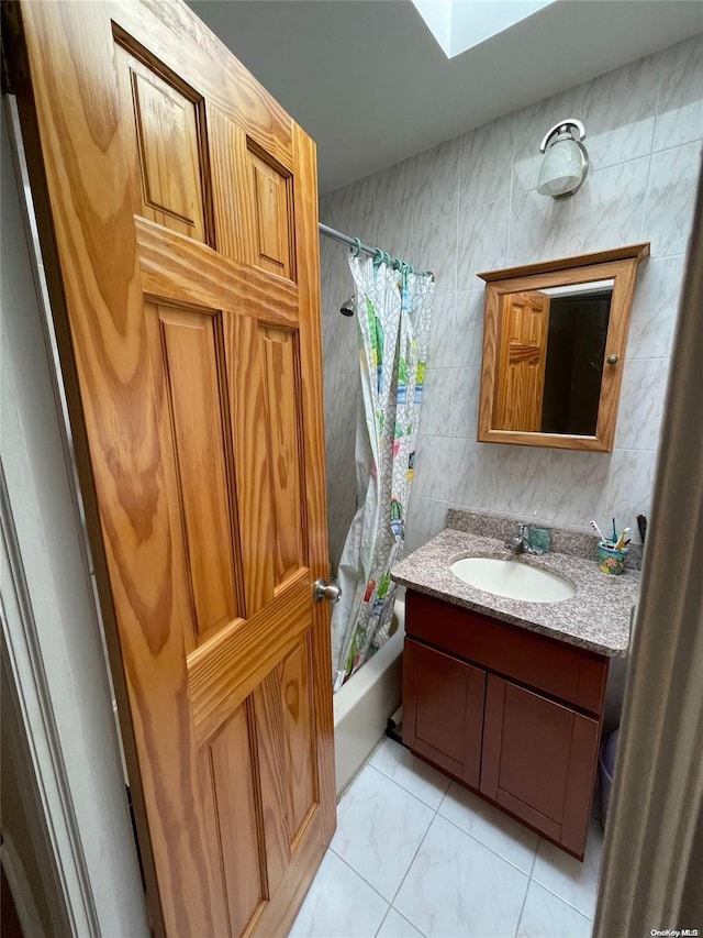 bathroom with vanity, shower / bathtub combination with curtain, a skylight, and tile walls