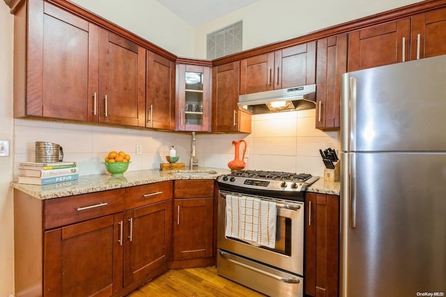 kitchen with light stone countertops, appliances with stainless steel finishes, light hardwood / wood-style floors, and sink