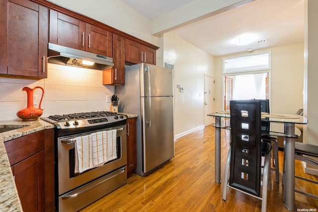 kitchen with wood-type flooring, light stone countertops, stainless steel appliances, and tasteful backsplash